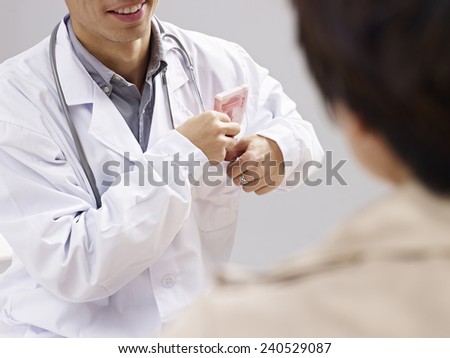 asian doctor putting kickback money in pocket.