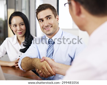 a caucasian businessman shaking hands with his asian partner before meeting.