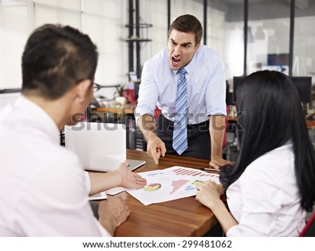 bad-tempered caucasian business executive yelling at two asian subordinates in office.