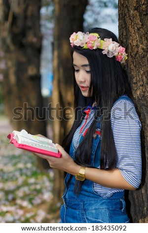 Young christian woman reading a bible under pink flower tree