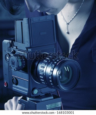 Woman photographer working with medium format camera on a tripod blue tone