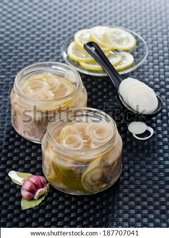 marinated mackerel slices in a glass jar with lemon onion garlic and spices on a black background