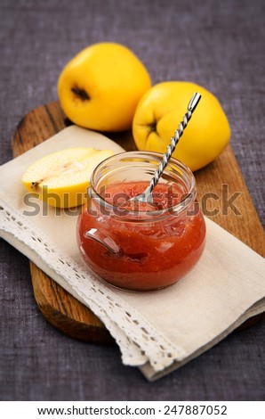 quince jam in a glass jar on a wooden board with quince fruits in the background