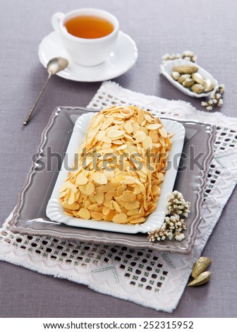 festive biscuit rolls with almond slices on a gray plate with a cup of tea in the background