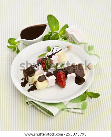 sweet fruit skewers with banana strawberry marshmallow drizzled with chocolate sauce and mint on a white plate