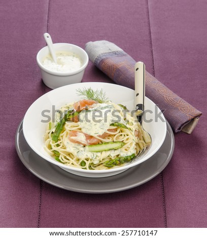 spaghetti with asparagus and salmon with sauce in white and gray plate on a purple tablecloth