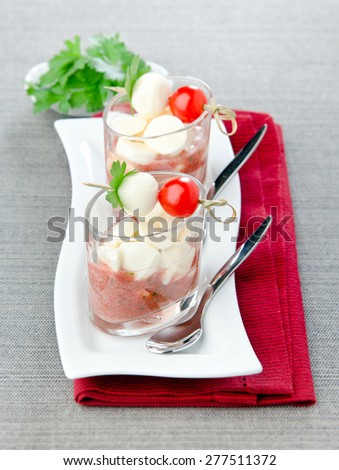 Snack tomato sauce in the cup cherry tomatoes with mozzarella skewers on a white plate gray tablecloth