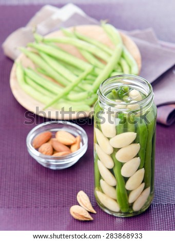 home-made canned Green beans with almonds in a glass jar on a purple background with nuts nearby and green beans in the background