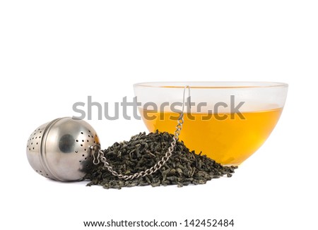 Glass piola bowl of tea next to metallic infuser and a pile of dried leaves isolated over white background