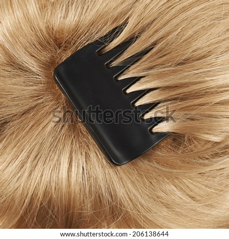 Open wave blond hair fragment with the black comb over it as a texture background composition