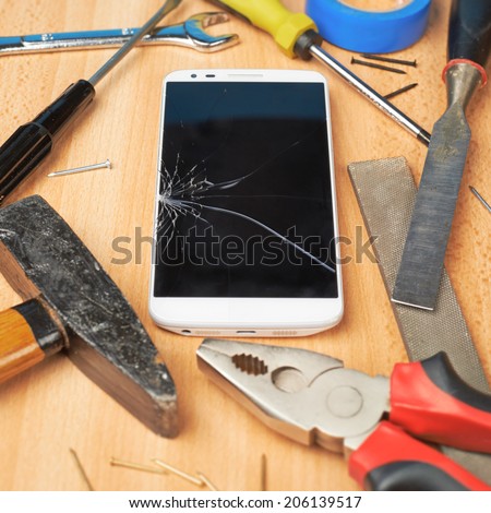 Repair mobile phone composition of a smartphone with a broken screen next to the multiple tools over a wooden surface