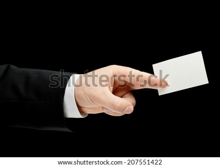 Caucasian male hand in a business suit, holding the white empty business card, low-key lighting composition, isolated over the black background