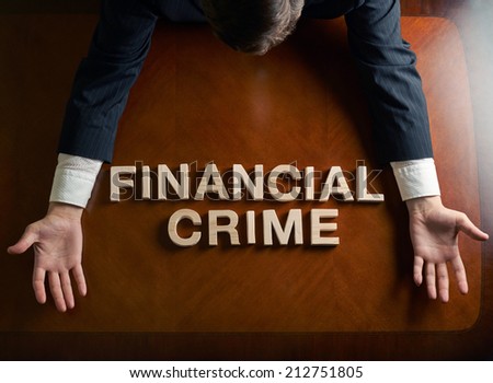 Phrase Financial Crime made of wooden block letters and devastated middle aged caucasian man in a black suit sitting at the table, top view composition with dramatic lighting
