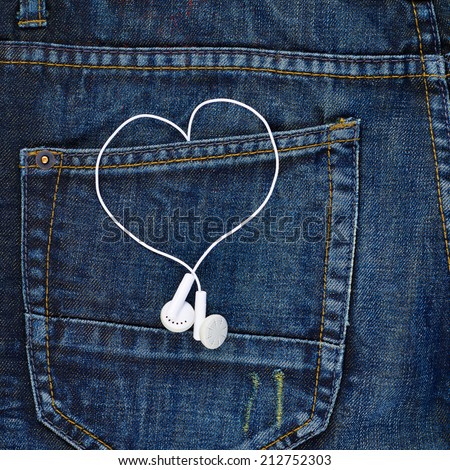 Pair of white ear-in headphones forming a heart shape in a back pocket of a navy blue denim jeans as a background composition