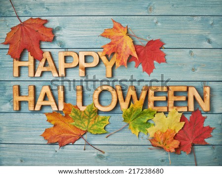 Happy Halloween composition made of maple leaves and wooden block letters over the background made of green pine wood boards