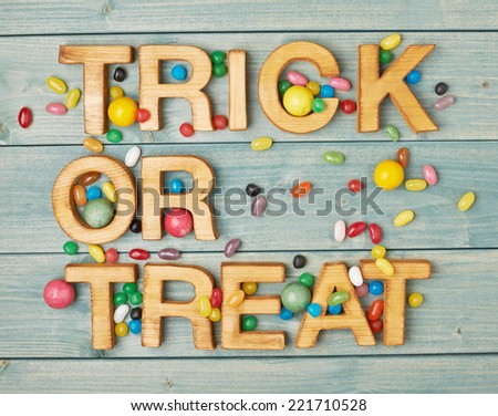 Trick or treat written with wooden letters and multiple candy sweets lying around over the covered with green boards surface composition