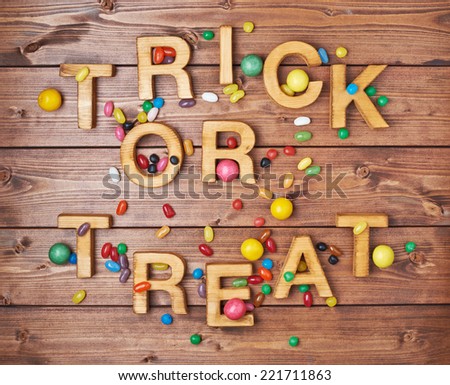 Trick or treat written with wooden letters and multiple candy sweets lying around over the covered with brown boards surface composition