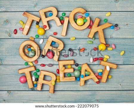 Trick or treat written with wooden letters and multiple candy sweets lying around over the covered with green boards surface composition