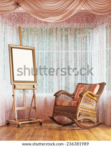 Copyspace empty picture frame on the wooden easel and next to wicker rocking chair, composition against the window\'s curtains background