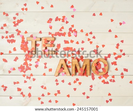 Te Amo meaning I Love You in Spanish written with the block letters covered with red heart shaped confetti over the wooden background
