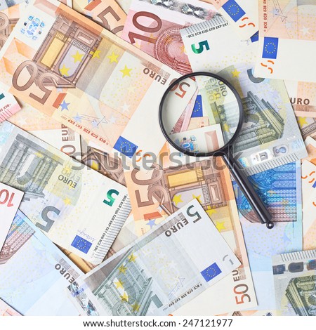 Magnifying glass over the surface covered with multiple euro bank note bills