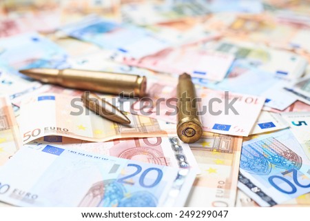 Few ammunition bullet shells over the surface covered with the multiple euro bank note bills