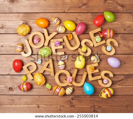 Words Joyeuses Paques as Happy Easter in french language made of wooden letters and surrounded with multiple egg decorations as a festive Easter background composition