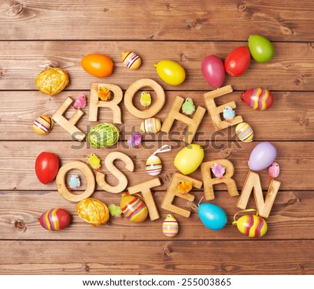 Words Frohe Ostern as Happy Easter in german language made of wooden letters and surrounded with multiple egg decorations as a festive Easter background composition