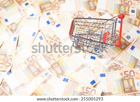 Tiny shopping cart over the surface covered with the multiple fifty euro bank notes