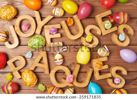 Words Joyeuses Paques as Happy Easter in french language made of wooden letters and surrounded with multiple egg decorations as a festive Easter background composition