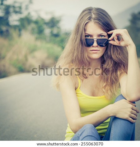 Trendy Hipster Girl in sunglasses Relaxing on the road near tree at the day time. Concept of Modern Youth Lifestyle.  Blowing Long Hair.