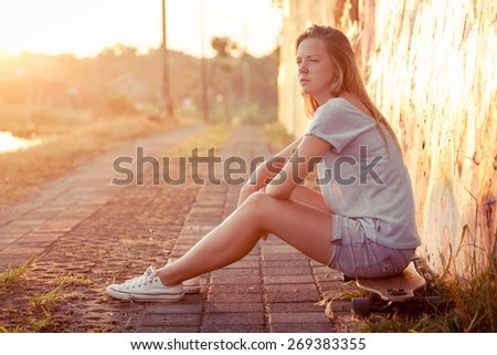 Fashion lifestyle, Beautiful young blonde woman with skateboard sitting near the wall with graffiti at the day time.