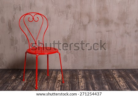Red metal chair in nterior room with gray decorative plaster wall and dark wooden floor