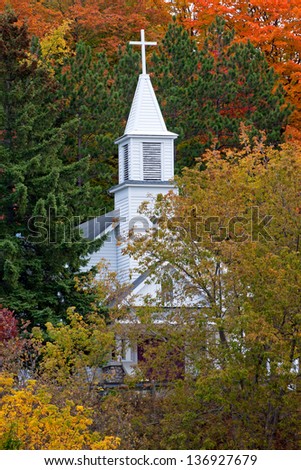 A white church steeple towers up into the autumn trees in Maple City Michigan. St. Rita\'s Catholic Church is a wonderful display in any season.