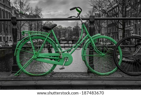 Green bike isolated on black and white over an Amsterdam canal. Very moody sky in background.