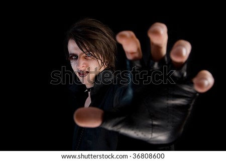 Gothic boy with artistic make-up and blue lenses stretching his hand, isolated on black background