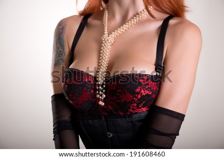 Busty redhead woman in vintage red bra, sheer gloves and pearl necklace