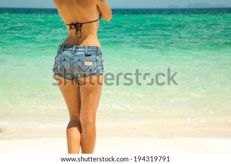 Young beautiful woman in denim shorts sunbathing on the beach