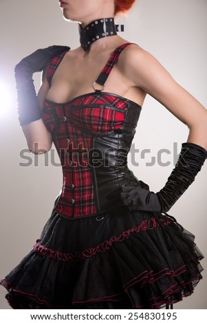 Attractive woman dressed in punk style, plaid leather corset and skirt, studio shot