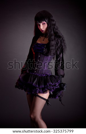 Cute witch in purple corset outfit for Halloween, studio shot