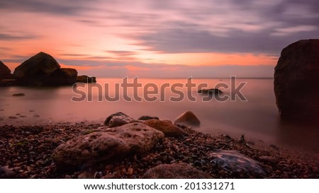 Beautiful ocean sunrise - calm sea and boulders stone coastline with unusual light