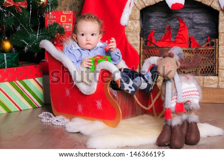 Beautiful curly-haired boy in a sleigh in the New Year fire