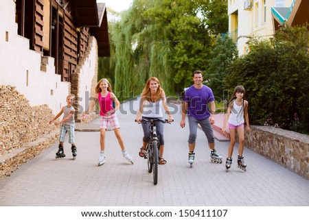people in the park on roller skates and bike. big sports family