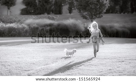 beautiful blond girl running in the park on a glade with a dog. black-and-white photo