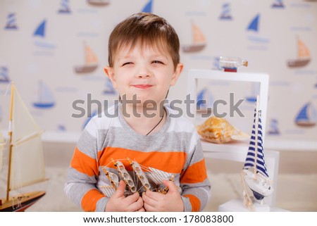 Small boy in striped shirt holds artificial wooden ship with paper sails