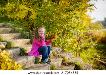 Adorable little girl with yellow leaves in hands. walking in the autumn park