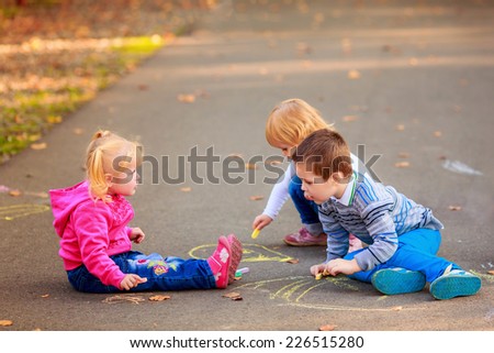 happy children draw colored chalk on the asphalt in the park
