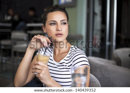 alone girl drink coffee with a tubule in a cafe and looking to the side