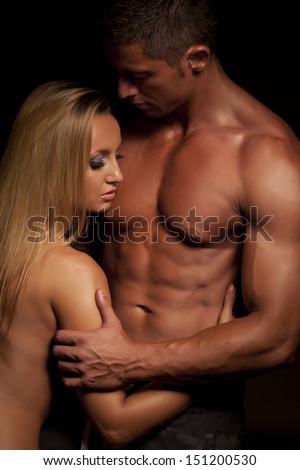 Young and fit topless couple in an embrace on dark background
