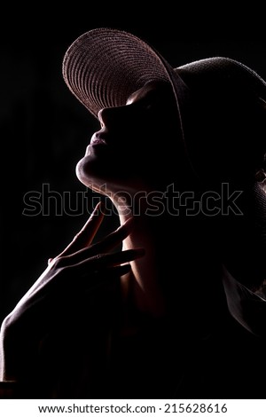unknown woman with a hat and face in shadow touching her neck